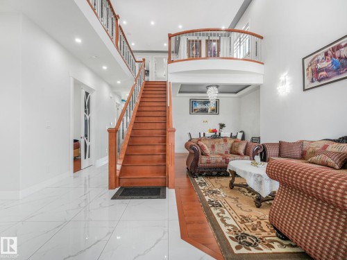 Two-story foyer featuring a grand staircase with wood railings, white tile flooring, and recessed lighting - 120 38 Street Sw, Edmonton, AB 