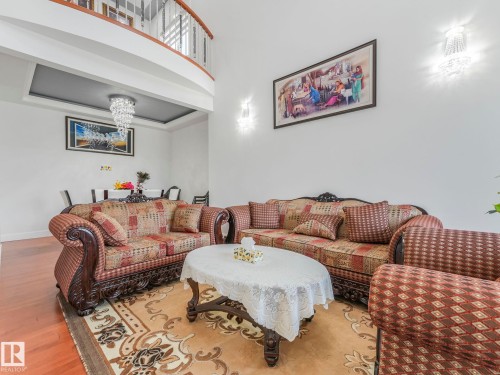 Hardwood flooring, recessed ceiling with chandelier, curved balcony with metal balusters, and wall-mounted sconces - 120 38 Street Sw, Edmonton, AB 