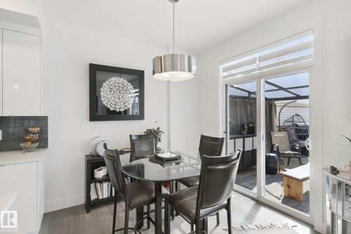 Sliding glass door leading to an outdoor covered patio, contemporary pendant lighting, wood-finish flooring, white walls, and built-in cabinetry - 153 Cavanagh Common Sw, Edmonton, AB 