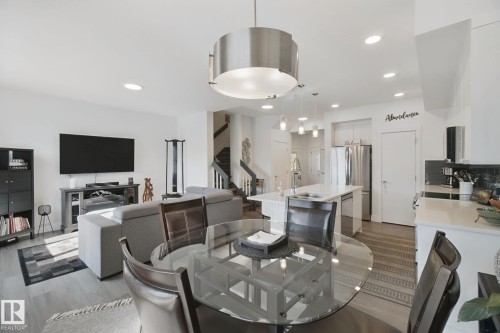Open-concept living space featuring wood-finish flooring, a contemporary kitchen island with a sink, stainless steel appliances, and recessed lighting throughout - 153 Cavanagh Common Sw, Edmonton, AB 