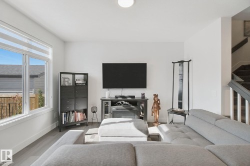 White walls, wood-finish flooring, large window with blinds, recessed lighting, and a staircase with dark wood-finish treads - 153 Cavanagh Common Sw, Edmonton, AB 