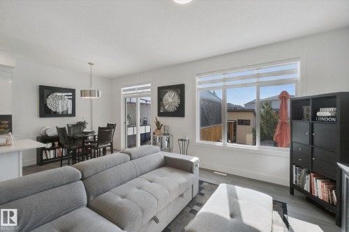Open-concept living area with wood-finish flooring, large windows, and a sliding glass door - 153 Cavanagh Common Sw, Edmonton, AB 