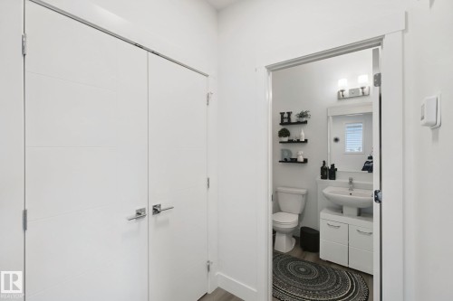 Recessed lighting, wood-finish flooring, white paneled doors with chrome hardware, white vanity with integrated sink, and wall-mounted light fixture - 153 Cavanagh Common Sw, Edmonton, AB 