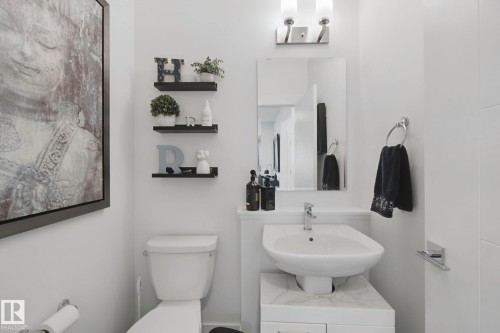 White pedestal sink with a single-handle chrome faucet, rectangular mirror, and a two-bulb vanity light fixture - 153 Cavanagh Common Sw, Edmonton, AB 