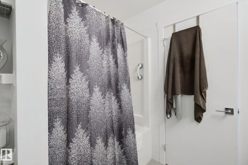 Shower enclosure with a white grab bar and a modern white door featuring a chrome lever handle - 153 Cavanagh Common Sw, Edmonton, AB 
