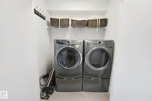 Dedicated laundry area featuring front-loading washer and dryer, elevated on pedestals - 153 Cavanagh Common Sw, Edmonton, AB 