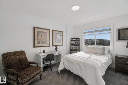 Room featuring light gray carpeting, a large window with roller shades, and a white desk - 153 Cavanagh Common Sw, Edmonton, AB 