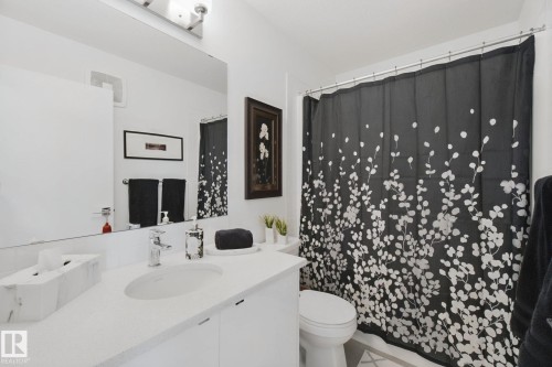 White vanity with integrated sink, chrome faucet, wall-mounted mirror, and overhead light fixture - 153 Cavanagh Common Sw, Edmonton, AB 