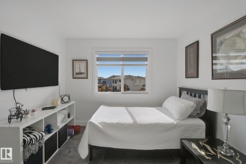 White walls with a window featuring blinds, dark wood-finish flooring, and a built-in shelving unit - 153 Cavanagh Common Sw, Edmonton, AB 