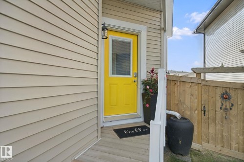 Yellow entry door with white trim, exterior wall with horizontal siding, and a wooden fence - 153 Cavanagh Common Sw, Edmonton, AB 