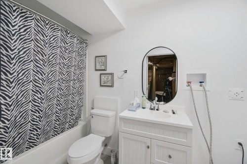 Bathroom featuring a white vanity with integrated sink, oval mirror, bathtub with shower, and toilet - 153 Cavanagh Common Sw, Edmonton, AB 