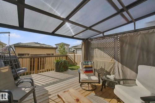 Wood-finish deck with a transparent roof structure, lattice privacy screen, and a surrounding wood fence - 153 Cavanagh Common Sw, Edmonton, AB 