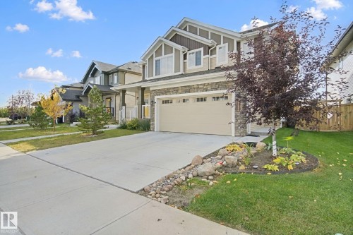 Stone and siding exterior with a multi-pane window design, two-car garage, and concrete driveway - 153 Cavanagh Common Sw, Edmonton, AB 