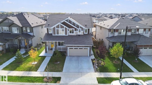 Stone facade with horizontal siding accents, attached garage, concrete driveway, and front porch - 153 Cavanagh Common Sw, Edmonton, AB 