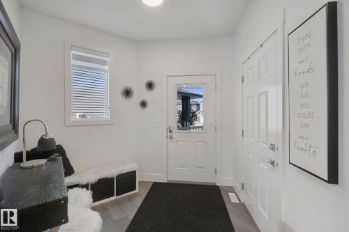Bright entry featuring wood-finish flooring, a white paneled door with frosted glass, and a second white paneled door - 153 Cavanagh Common Sw, Edmonton, AB 