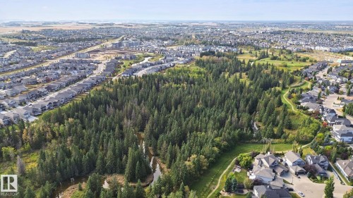 Expansive parkland with mature trees, winding pathways, and a natural water feature, surrounded by residential properties - 153 Cavanagh Common Sw, Edmonton, AB 