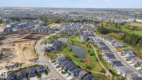 Aerial perspective highlighting a residential development with a central pond and green spaces, surrounded by established neighborhoods and new construction areas - 153 Cavanagh Common Sw, Edmonton, AB 