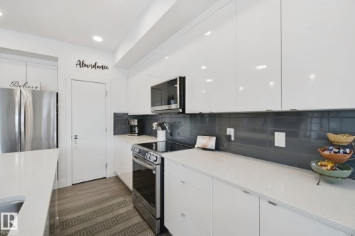 White high-gloss cabinetry, stainless steel appliances, light-toned countertops, gray subway tile backsplash, and wood-finish flooring - 153 Cavanagh Common Sw, Edmonton, AB 