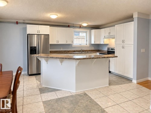 Kitchen featuring white cabinetry, a large kitchen island, stainless steel refrigerator, and a built-in range - 18929 99A Avenue Nw, Edmonton, AB 