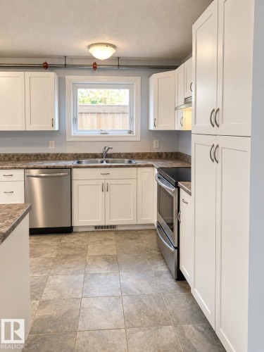 Kitchen featuring white shaker-style cabinetry, stainless steel appliances, a double basin sink, and a multi-tone countertop - 18929 99A Avenue Nw, Edmonton, AB 