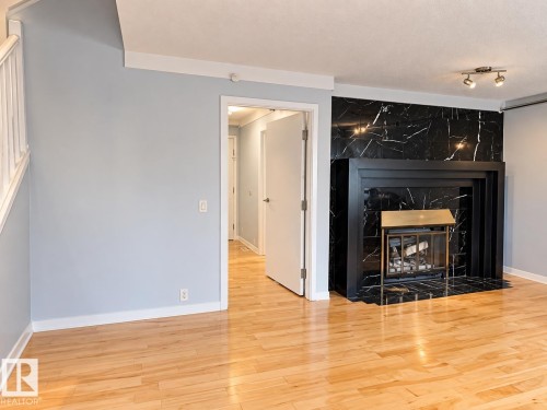 Hardwood flooring, black marble-look fireplace surround, integrated fireplace screen, white trim, and track lighting - 18929 99A Avenue Nw, Edmonton, AB 