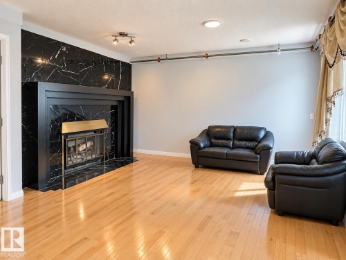 Hardwood flooring, black fireplace surround with black mantel, black marble-style wall paneling, and track lighting - 18929 99A Avenue Nw, Edmonton, AB 