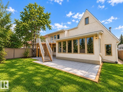 Expansive rear yard featuring a large green lawn, a ground-level patio with light-toned pavers, and a raised wood deck with staircase access - 18929 99A Avenue Nw, Edmonton, AB 