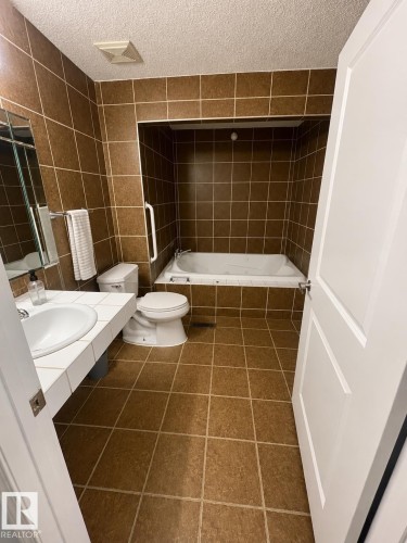 Brown square tile flooring, brown square tile walls, built-in bathtub, white toilet, white vanity with integrated sink - 18929 99A Avenue Nw, Edmonton, AB 