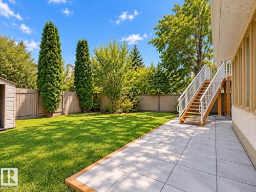 Expansive backyard featuring a manicured lawn, full privacy fencing, mature trees, a storage shed, and a tiled patio with a wood staircase - 18929 99A Avenue Nw, Edmonton, AB 
