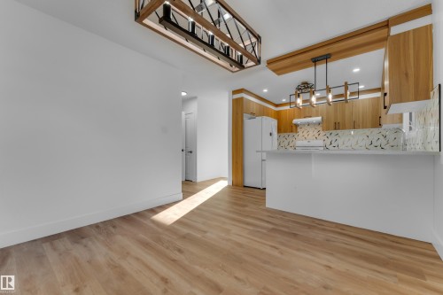 Wood-finish flooring, white walls, kitchen island with a white countertop, wood cabinetry, and a geometric backsplash - 52314 Rge Road 215, Rural Strathcona County, AB 