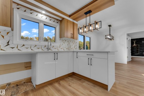 Contemporary kitchen featuring white cabinetry with black hardware, wood-finish flooring, a geometric tile backsplash, and a window above the sink - 52314 Rge Road 215, Rural Strathcona County, AB 