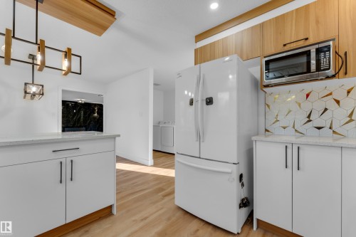 Wood-finish flooring, white cabinetry with black hardware, light-toned countertops, geometric tile backsplash, and overhead wood-finish cabinetry - 52314 Rge Road 215, Rural Strathcona County, AB 