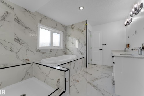 Spacious bathroom with large format tile flooring and wall coverings, a built-in soaking tub, a shower stall with a white pan, and a double vanity with undermount sinks - 52314 Rge Road 215, Rural Strathcona County, AB 