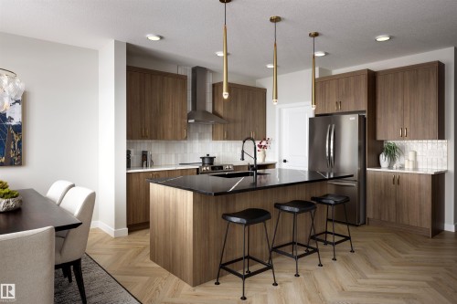 Kitchen featuring a large island with dark countertop, stainless steel appliances, wood-finish cabinetry, and chevron-patterned flooring - 16 Clichy Close, St. Albert, AB 