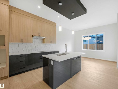 Kitchen featuring a central island with sink, light wood-finish flooring, two-tone cabinetry, and pendant lighting - 22 Dalquist Bay, Leduc, AB 