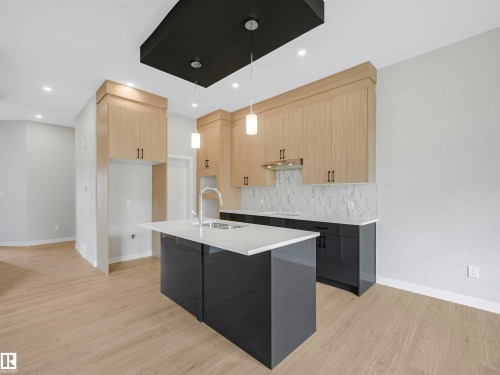 Kitchen featuring wood-finish cabinetry, a large center island with a white countertop, stainless steel sink with a pull-down faucet, and contemporary pendant lighting - 22 Dalquist Bay, Leduc, AB 