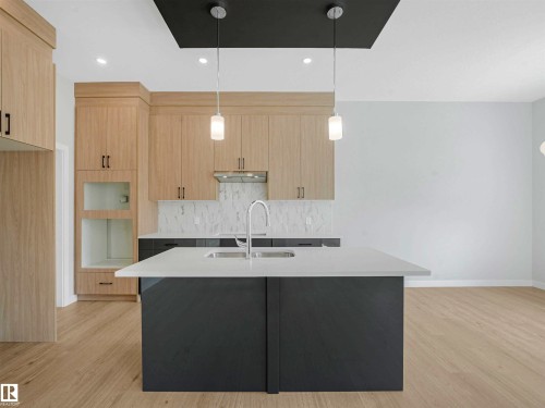 Kitchen featuring wood-finish cabinetry, a large center island with an integrated sink, a light-toned countertop, and recessed lighting with pendant fixtures - 22 Dalquist Bay, Leduc, AB 