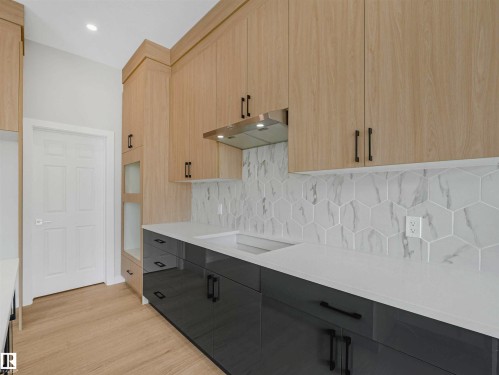 Light wood-finish upper cabinetry, grey lower cabinetry, white stone countertops, and a white hexagonal tile backsplash - 22 Dalquist Bay, Leduc, AB 
