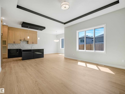 Open-concept layout with wood-finish flooring, recessed ceiling details, and a contemporary kitchen featuring light wood cabinetry, a central island, and a tile backsplash - 22 Dalquist Bay, Leduc, AB 