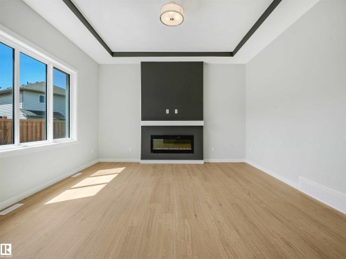 Recessed ceiling detail, wood-finish flooring, built-in electric fireplace, large windows, and a ceiling-mounted light fixture - 22 Dalquist Bay, Leduc, AB 