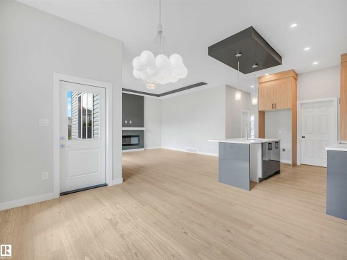 Open-concept living space with light wood-finish flooring, a contemporary kitchen island with a light-colored countertop, and modern pendant lighting - 22 Dalquist Bay, Leduc, AB 