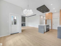 Open-concept living space with light wood-finish flooring, a contemporary kitchen island with a light-colored countertop, and modern pendant lighting - 