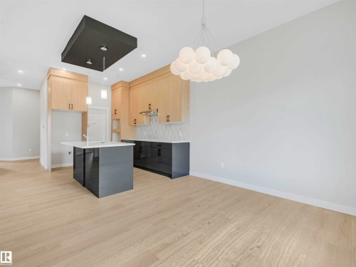 Kitchen featuring light wood-finish cabinetry, a central island with a white countertop, and a decorative ceiling light fixture - 22 Dalquist Bay, Leduc, AB 