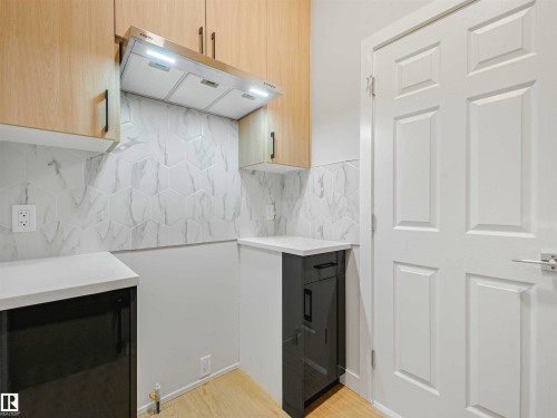 Light wood-finish upper cabinetry, white countertops, stainless steel range hood, hexagonal tile backsplash, and wood-finish flooring - 22 Dalquist Bay, Leduc, AB 