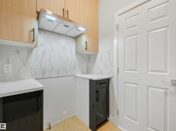 Light wood-finish upper cabinetry, white countertops, stainless steel range hood, hexagonal tile backsplash, and wood-finish flooring - 