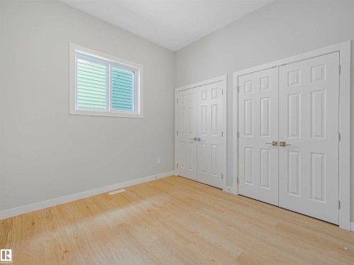 Light wood-finish flooring complemented by white walls, a white-framed window with horizontal blinds, and two sets of white paneled bifold doors - 22 Dalquist Bay, Leduc, AB 
