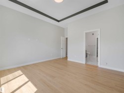 Recessed ceiling design, light wood-finish flooring, white walls, flush mount lighting, and white interior doors - 