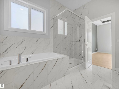 Built-in soaking tub with polished chrome fixtures, glass-enclosed shower, large format marble-look tile flooring, matching marble-look tile bath surround, and a double-pane window - 22 Dalquist Bay, Leduc, AB 