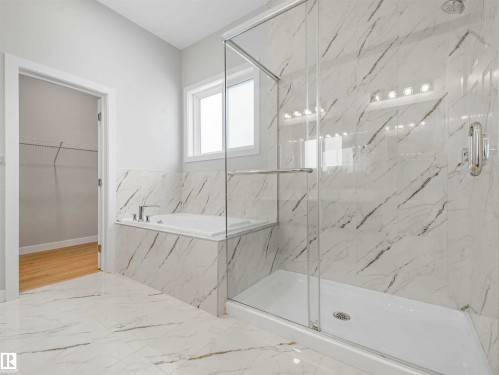 Spacious bathroom featuring a glass-enclosed shower, built-in bathtub, window, and full-height tile surround - 22 Dalquist Bay, Leduc, AB 
