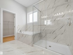 Spacious bathroom featuring a glass-enclosed shower, built-in bathtub, window, and full-height tile surround - 